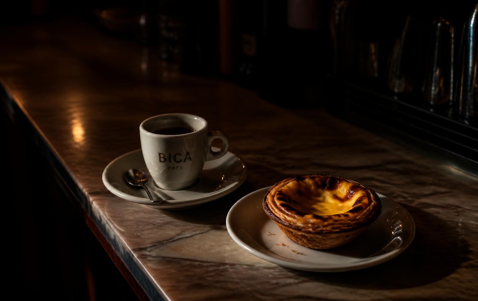 A pastel de nata beside an espresso bica on a marble counter